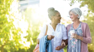 Two Women Walk Through a Park Together Drinking Coffee
