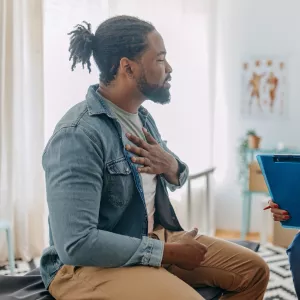 A Patient Holds His Hand to His Chest as He Consults with His Physician in a Doctor's Office. 