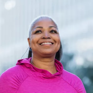A smiling woman outside wearing a pink shirt for breast cancer awareness.