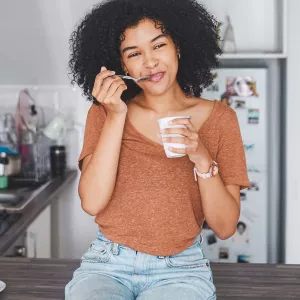 A woman sitting on her counter eating yogurt.