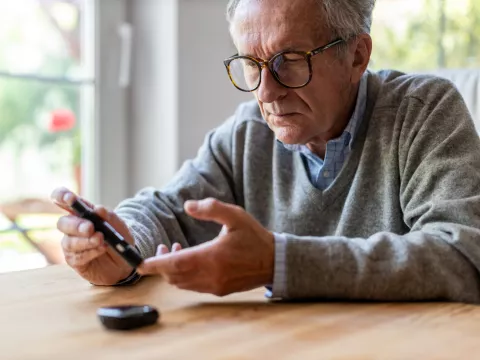 A Senior Checks His Glucose Levels with a Device While Sitting at the Kitchen Table