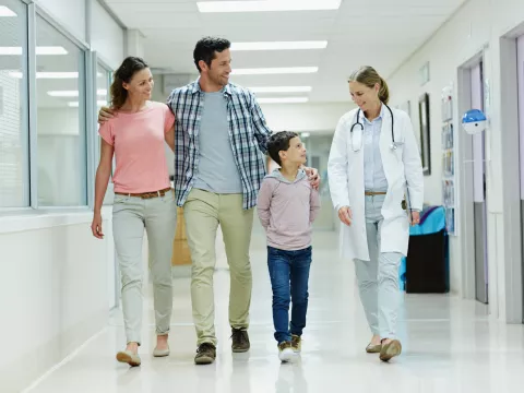 A Smiling Mother, Father and Son Walk Down a Hospital Hallway with a Doctor.