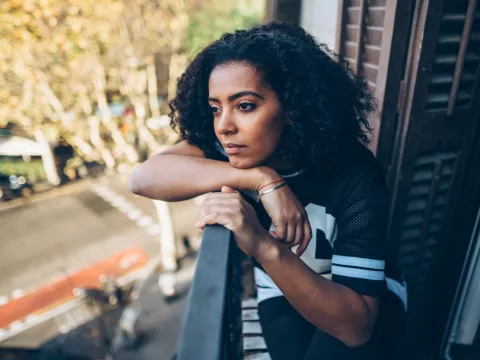 A Woman With a Concerned Look on Her Face Stares at Street From Her Balcony.