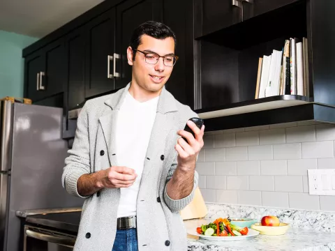 A Man Wearing Glasses Checks His Glucose Levels Before Eating a Healthy Meal in His Kitchen