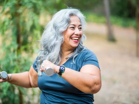 An overweight senior hispanic woman uses weights while she exercises