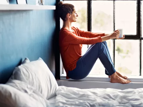 A woman sitting on a windowsill drinking tea.