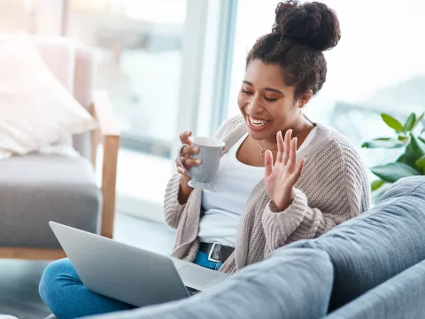 A woman waving to a friend on a video call. 