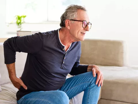 A senior gentleman showing discomfort while getting up from his couch