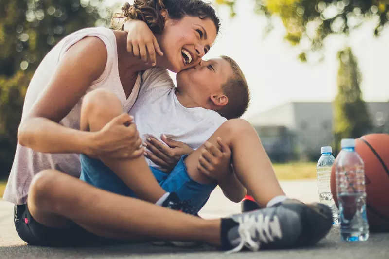 A mother and son take a water break on the basketball court during the summer.