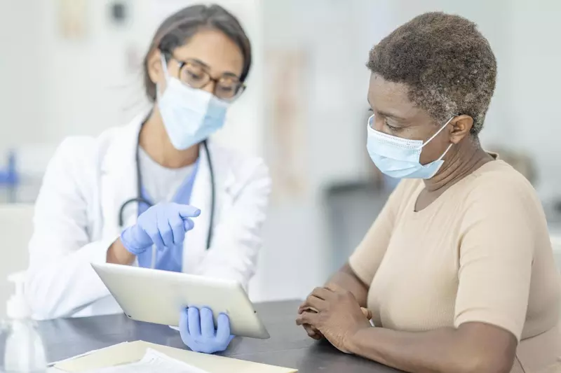 Older black woman talking with female doctor wearing masks