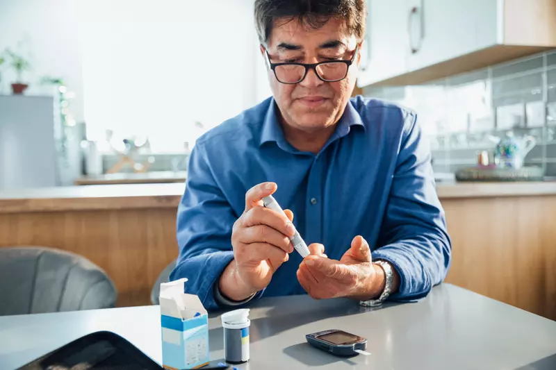 A man sitting in a kitchen using a glucose monitor.