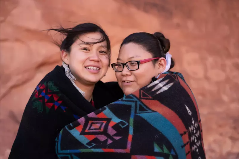 Native American mother and daughter wrapped in a blanket together while outdoors.