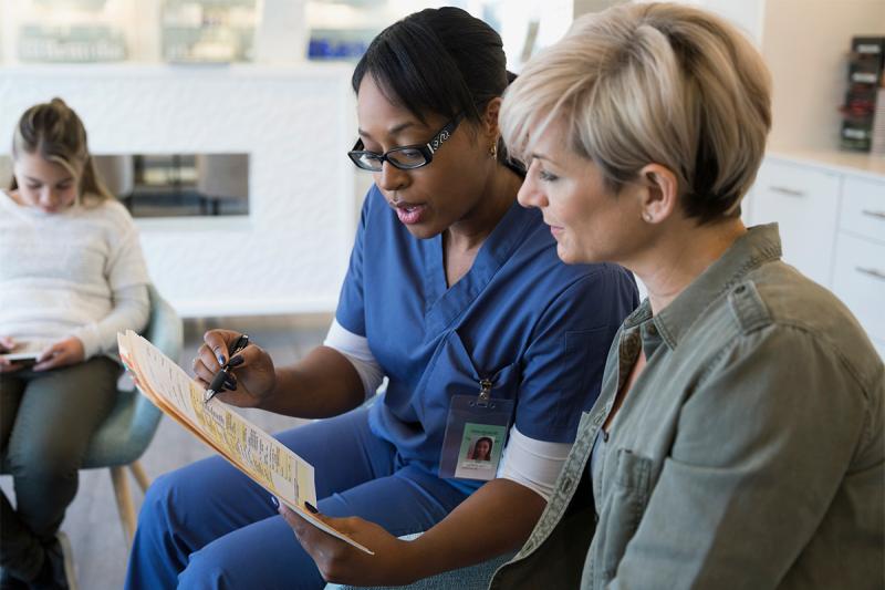 An African American nurse consults with a Caucasian female regarding her diagnosis.
