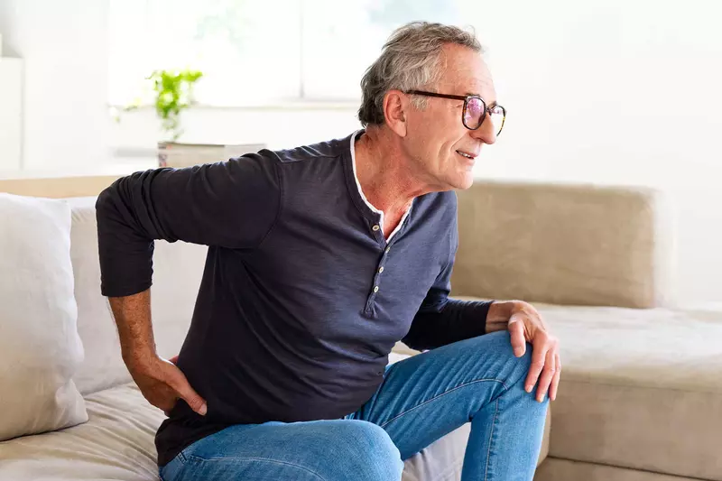 A senior gentleman showing discomfort while getting up from his couch