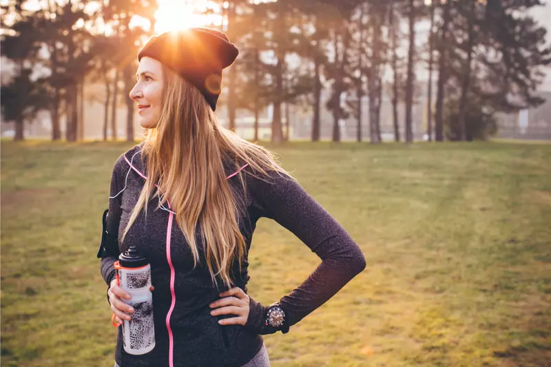 Woman wearing active wear and holding a water bottle in a park during winter.