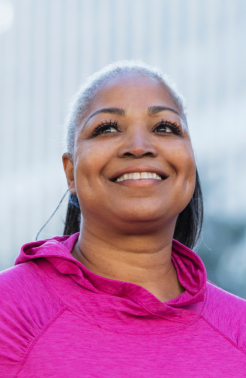 A smiling woman outside wearing a pink shirt for breast cancer awareness.