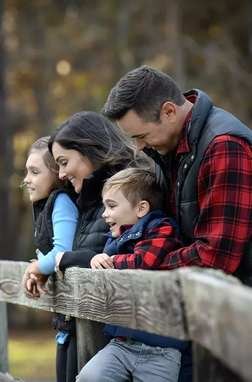 A family of four leaning on a fence while outdoors in the winter.