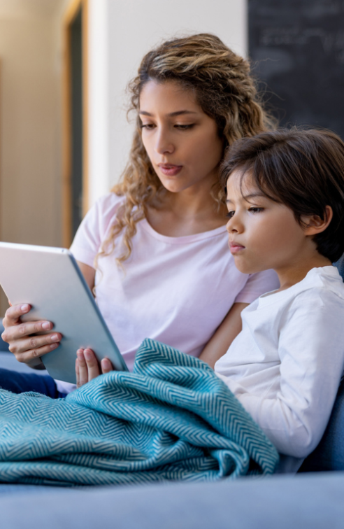 A mother and son sitting on a couch and using a tablet.