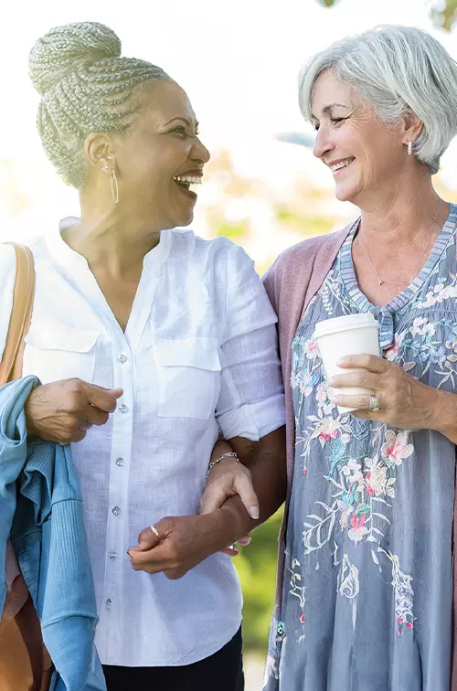 Two Women Walk Through a Park Together Drinking Coffee