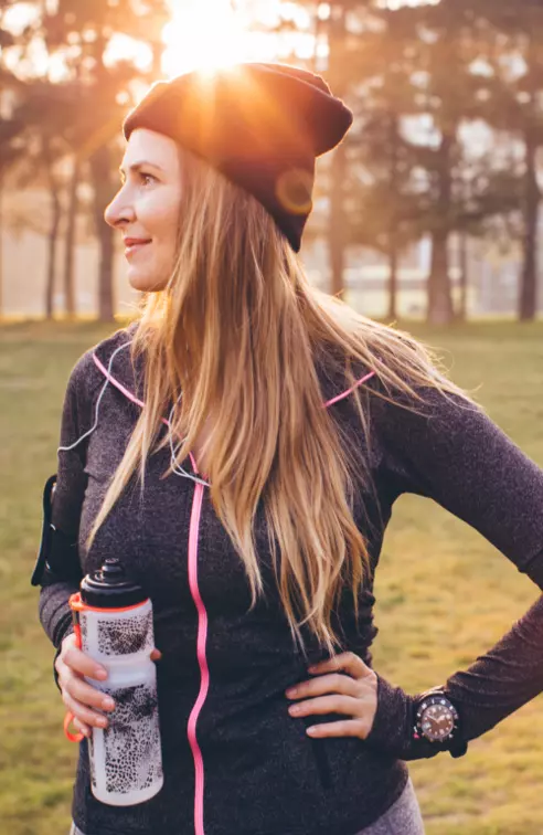 Woman wearing active wear and holding a water bottle in a park during winter.